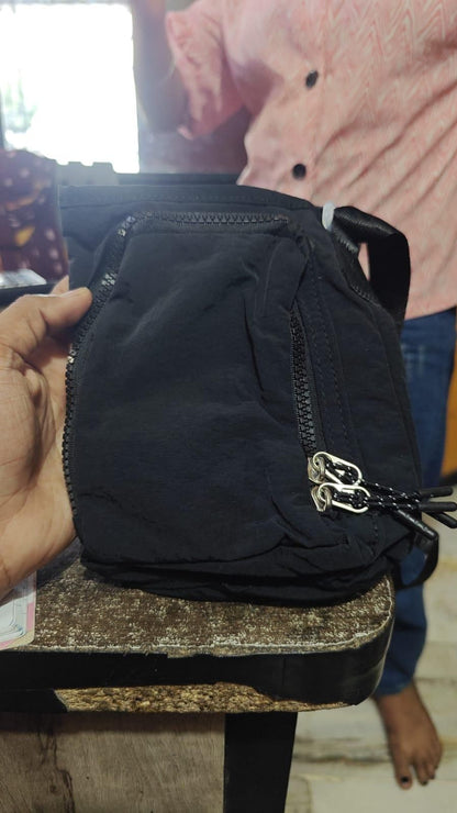 Black stylish side sling pouch with dual zipper pockets held in hand by person wearing pink shirt