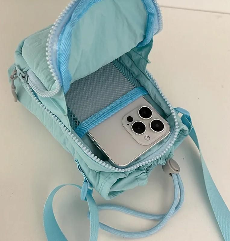Light blue stylish side sling pouch open with silver smartphone inside and adjustable strap